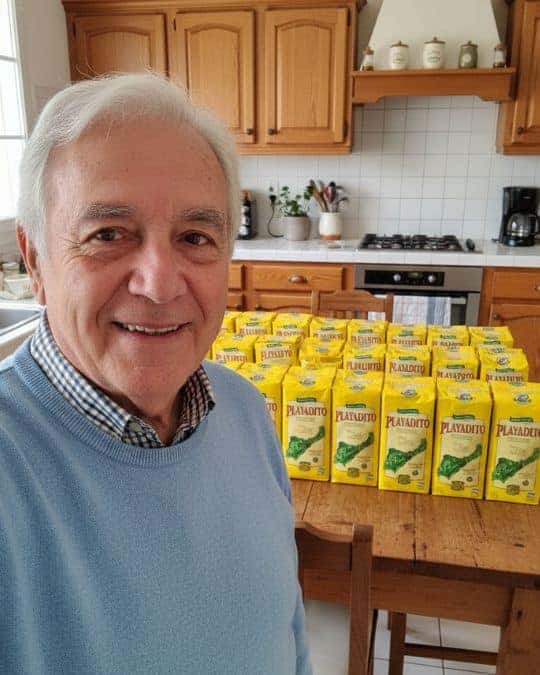Uomo sorridente con pacchi di Yerba Mate Playadito in cucina.