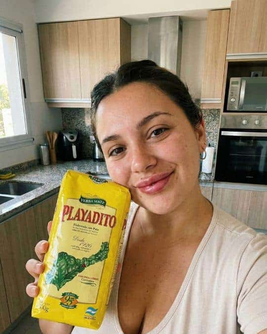 Donna sorridente con pacchetto di Yerba Mate Playadito in cucina moderna.