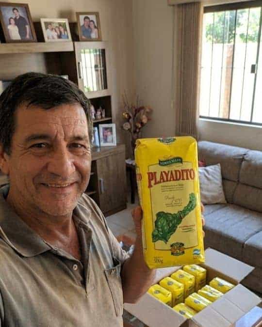 Uomo che mostra una confezione di yerba mate Playadito in salotto.