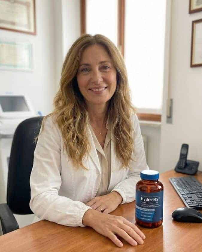 Donna sorridente con integratore Hydro-M5 su scrivania in ufficio.